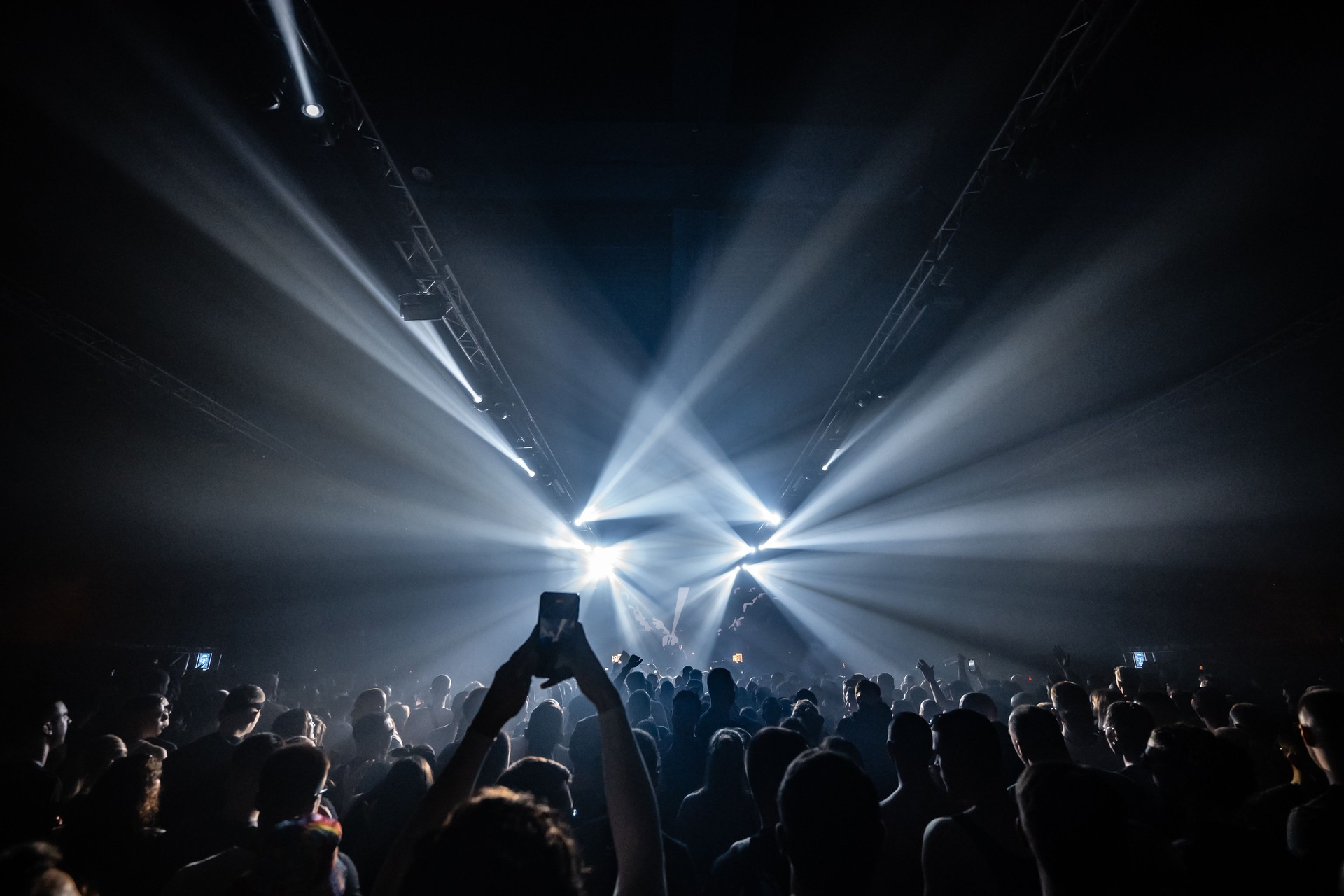 Crowd enjoying live music concert with bright stage lights illuminating dark arena
