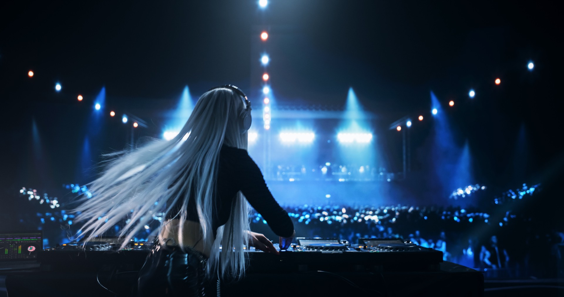 Female DJ Delivers a Live Performance of Electronic Music while Standing Behind Mixing Decks at a Massive Event. Colorful Lights and Dance Beats Play at an EDM Concert. Back View